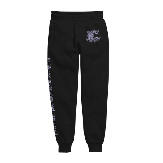 image of black sweatpants on a white background. small purple print on top right hip of the letter C. left leg has print down that says it's like we never knew each other at all